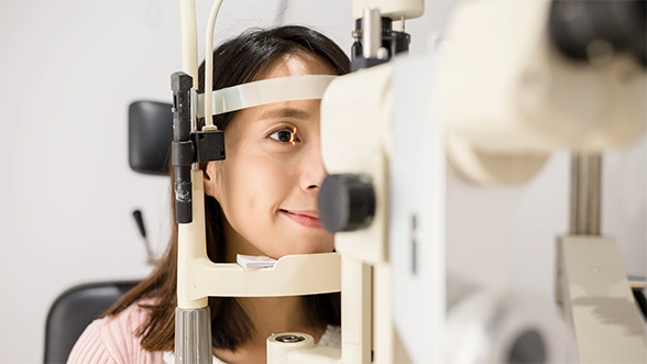 A person having an eye examination, positioned in front of an optical testing device called a slit lamp.